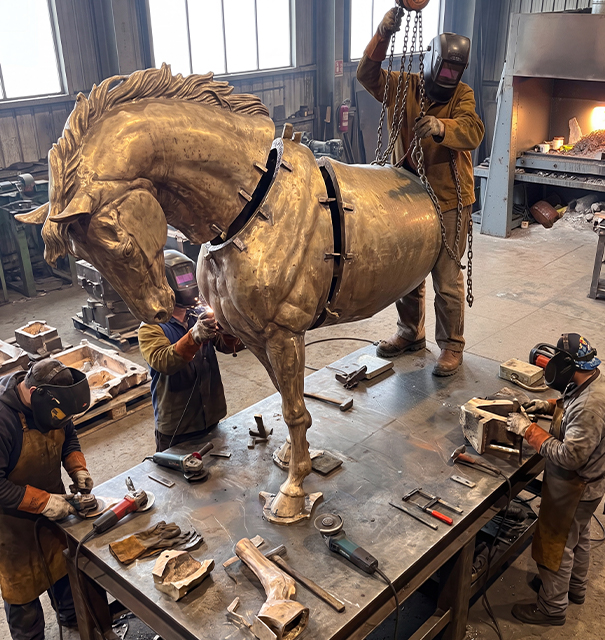 Artisans assemblant et soudant les différentes parties d’une sculpture de cheval en bronze